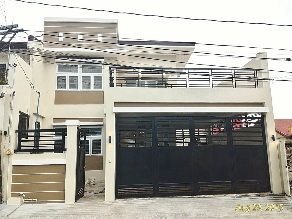 Completed house: a pale facade with sliding timber-louvred screens, a glazed balcony and a black metal railing.