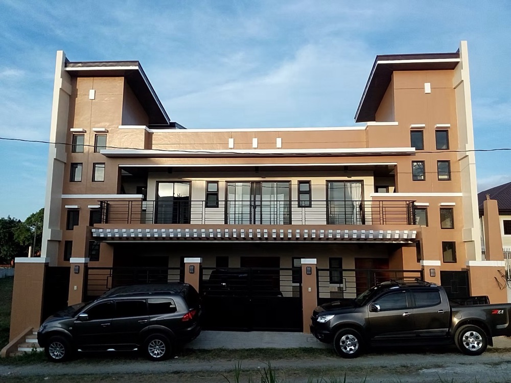 Completed house: a peach and cream facade with stacked balconies, dark louvred screens and a solid perimeter wall.