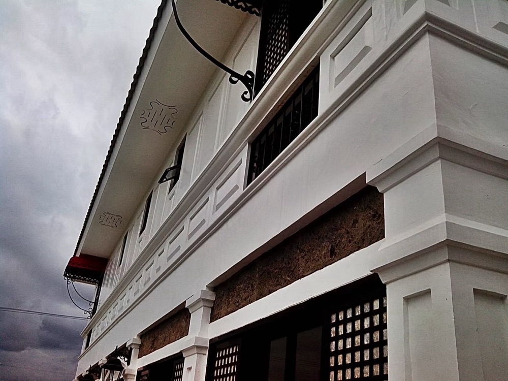 Close detail of the completed house: a moulded white cornice above a dark textured stone band and a banded window surround.