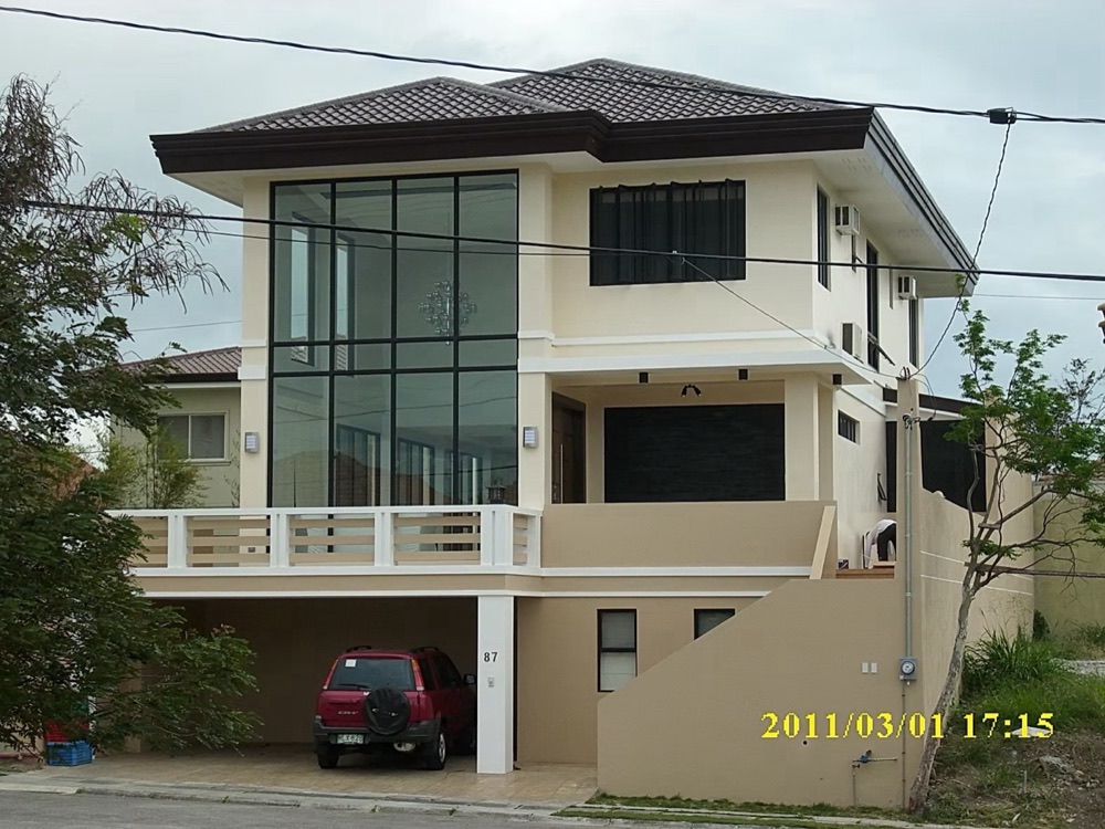 Completed house: a cream facade with full-height glazing across two storeys above a concrete balustrade.