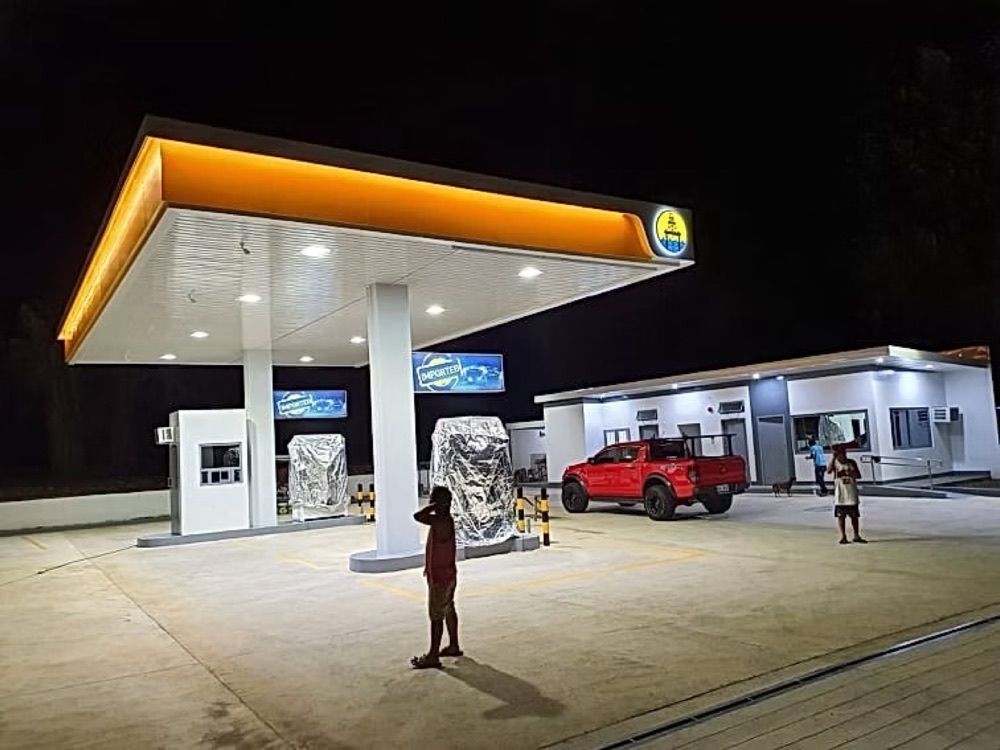 Completed station photographed at dusk: the canopy lit from beneath, dispensers and pumps on an empty forecourt.