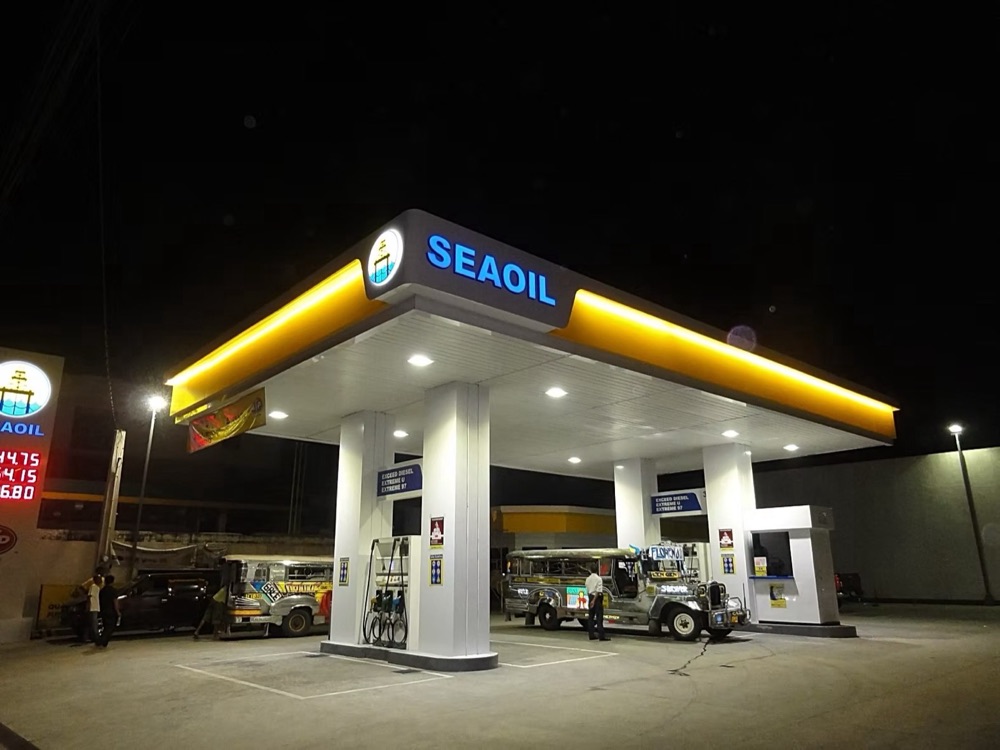 Completed station at night: a bright illuminated canopy above the pumps, with the price pylon lit at the roadside.