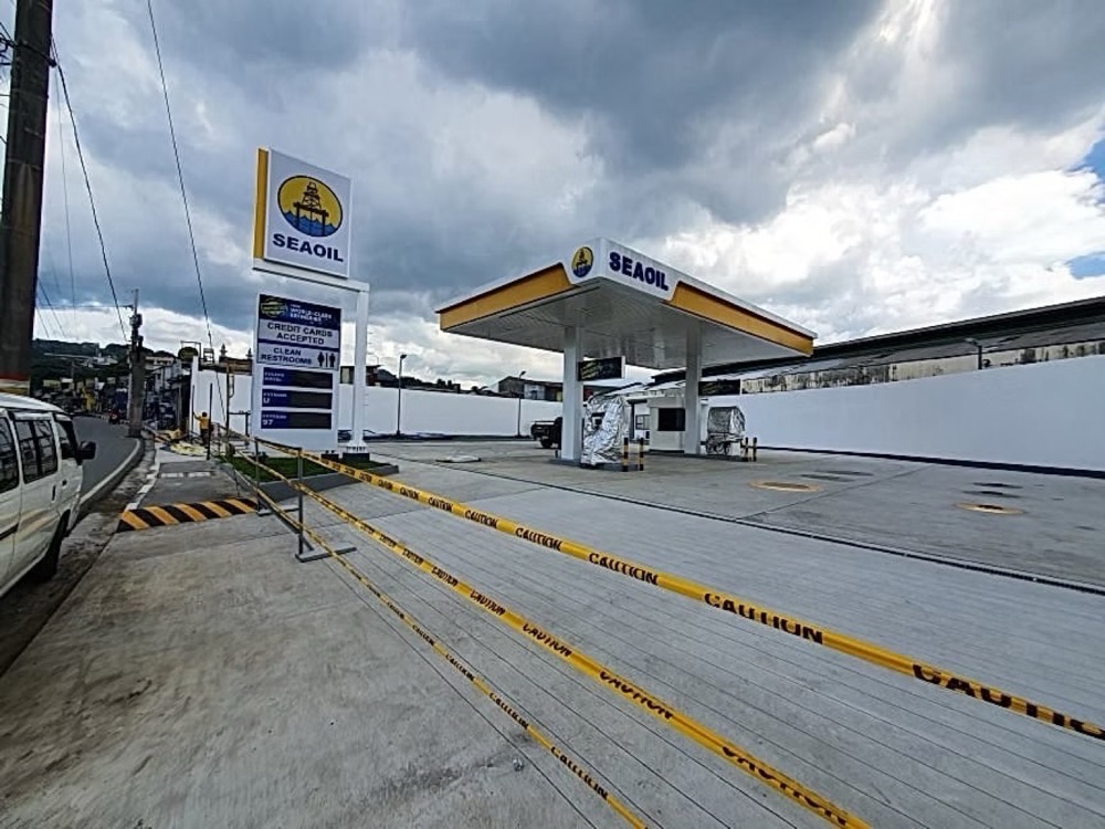Completed station beside a road: the branded canopy and pylon sign above the forecourt, with traffic passing.