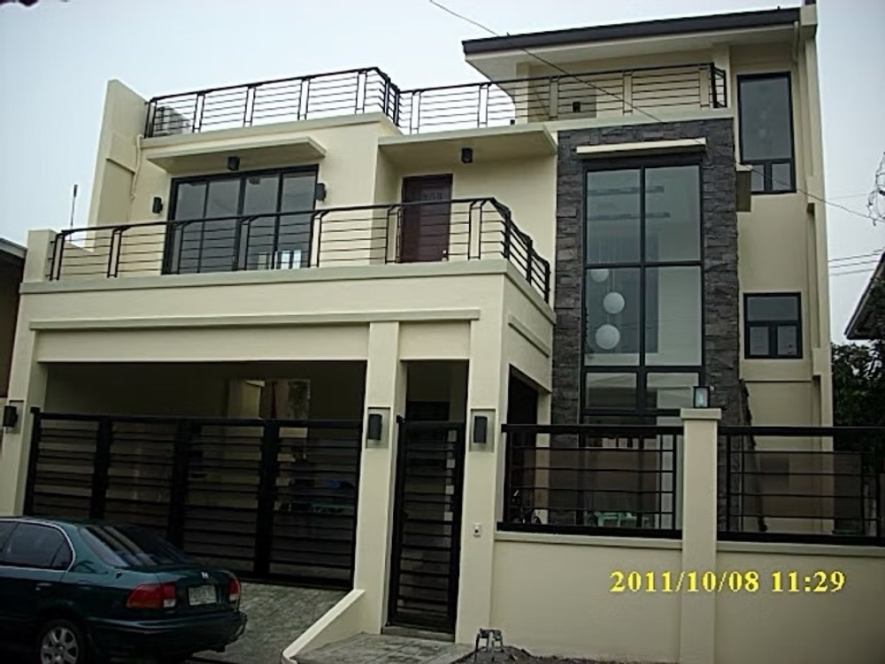 Completed house: a grey and white facade with a dark glazed upper storey behind a black metal railing above the garage.