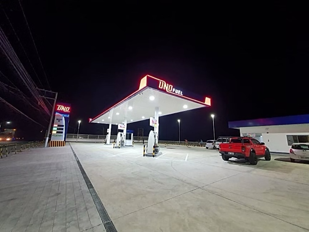 Completed station photographed at night, the canopy edge and pylon sign lit in red and white.
