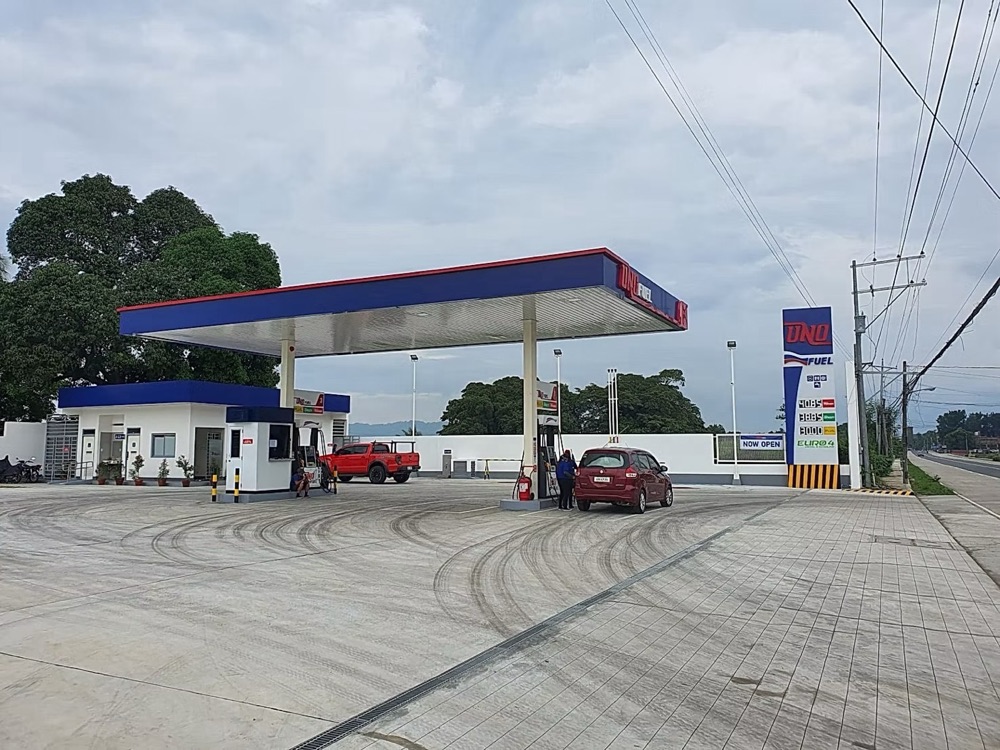 Completed station: canopy over the pump islands with a car at the pumps and the price pylon at the roadside.