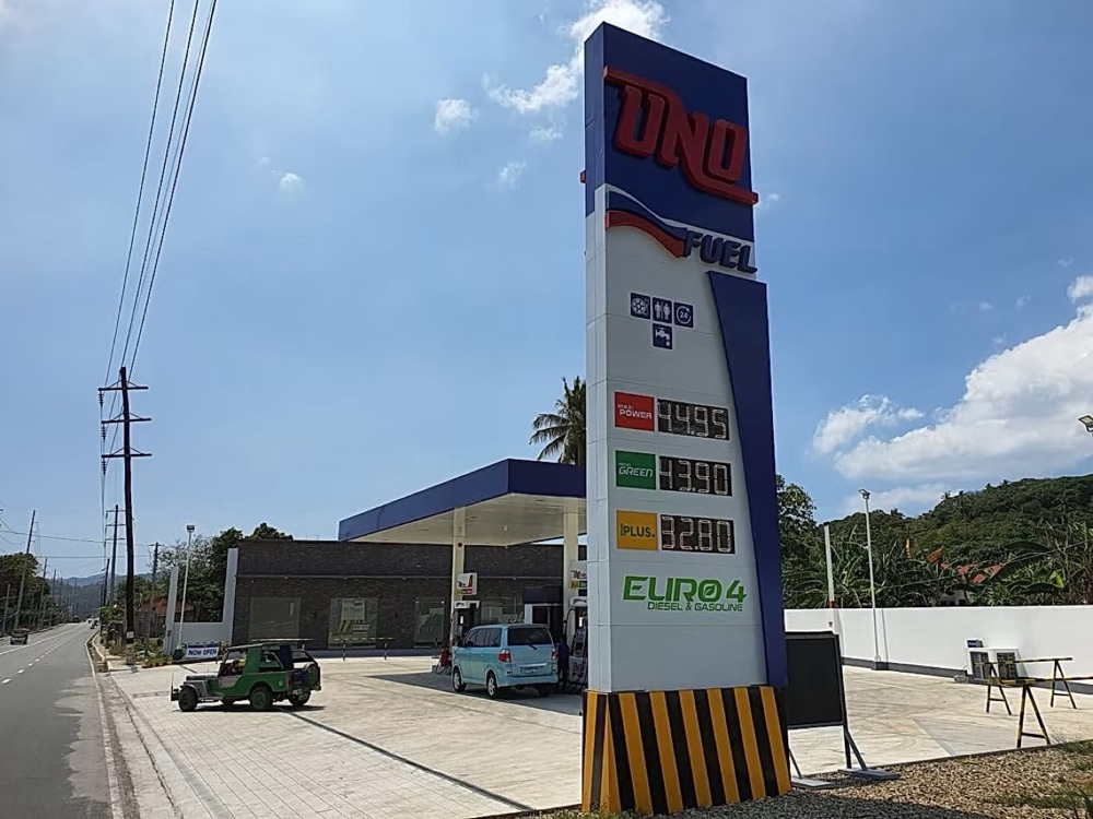 Completed station against a hillside, the price pylon listing fuel grades beside the canopy.