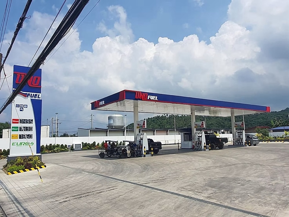 Completed station: the canopy and pumps with vehicles on the forecourt and the pylon sign at the entrance.