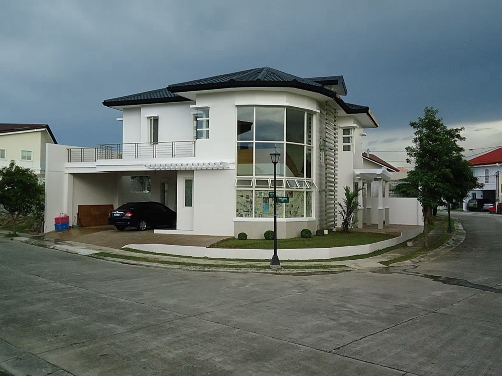 Finished two-storey house: white walls with grey stone accent panels, a curved glass bay window and a car port, seen from the street corner.